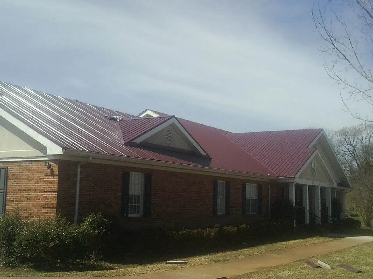 Red metal roof with gabled entries on a long brick building, from a Hail Damage Roof Repair job in Bokeelia