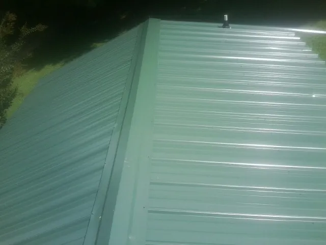 New green metal panels meeting at the ridge of a roof — Flat Roof Repair work by our crew in Bokeelia