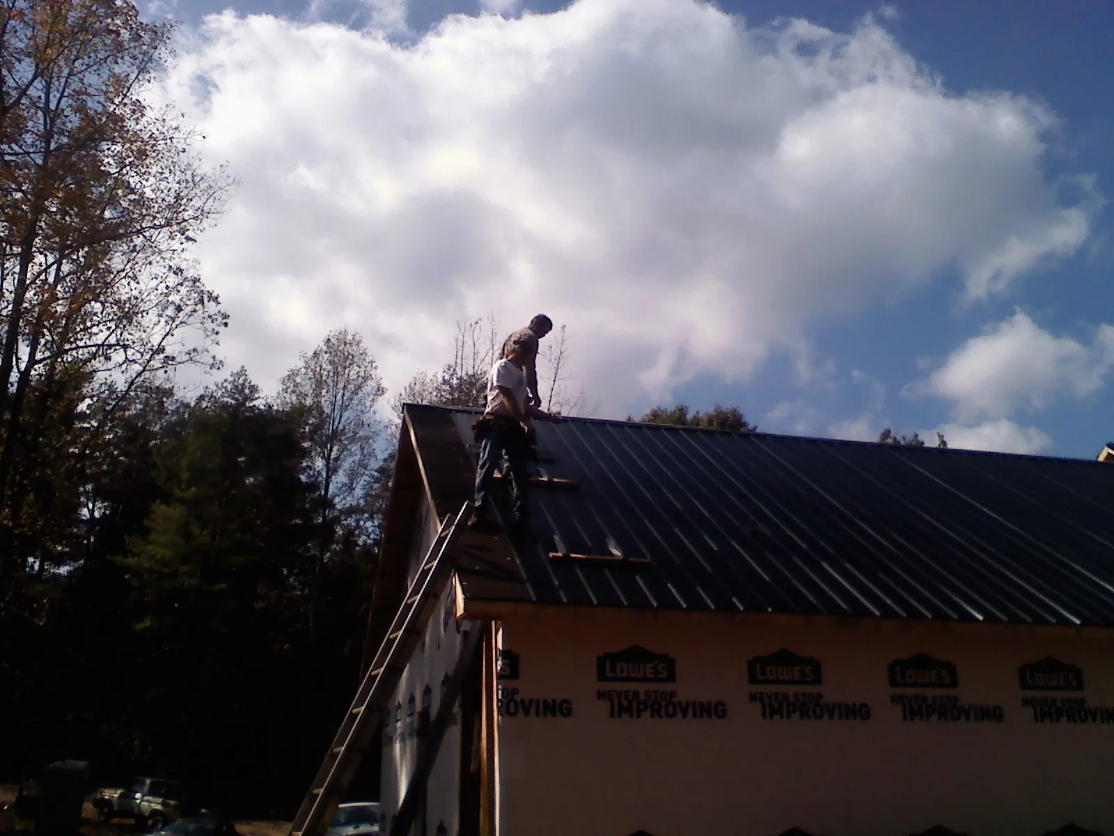 Roofer fastening dark metal panels high against a cloudy sky, from a Roof Inspection job in Bokeelia