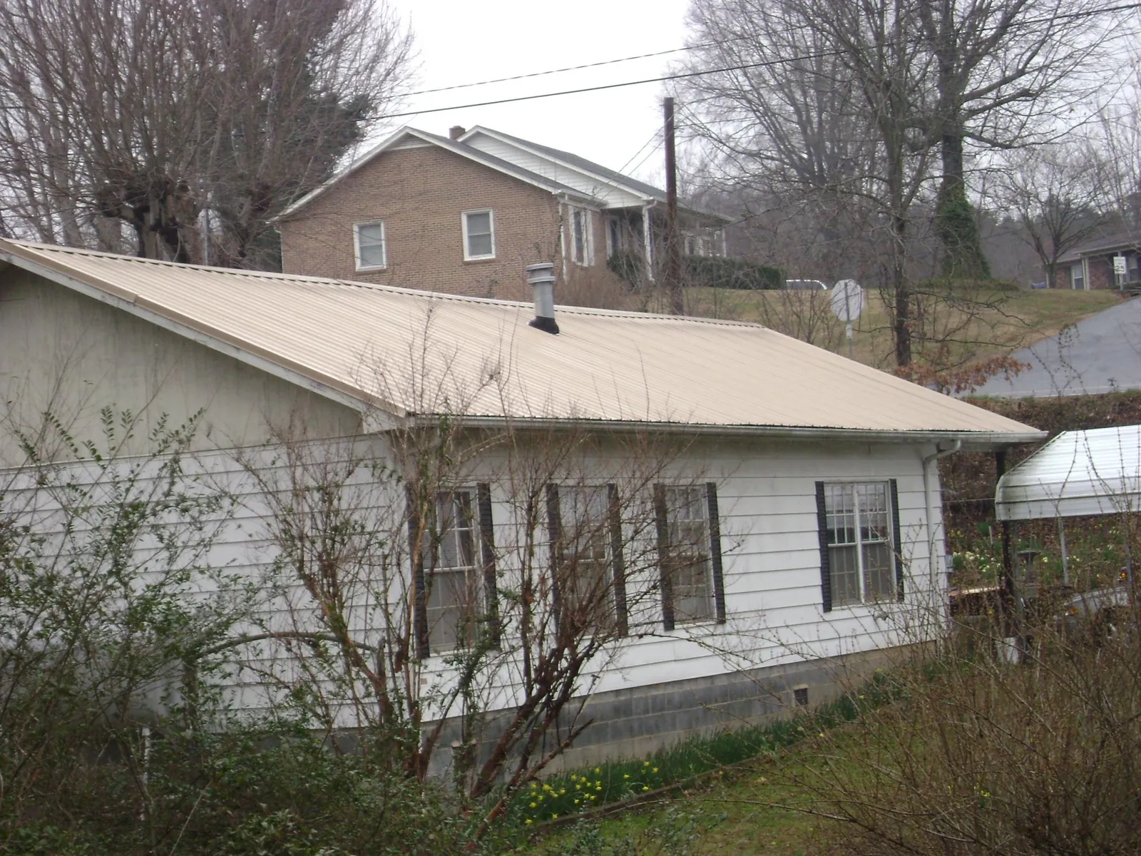Tan metal roof on a white sided house set into a hillside — Commercial Roofing by Roofing Brothers in Bokeelia